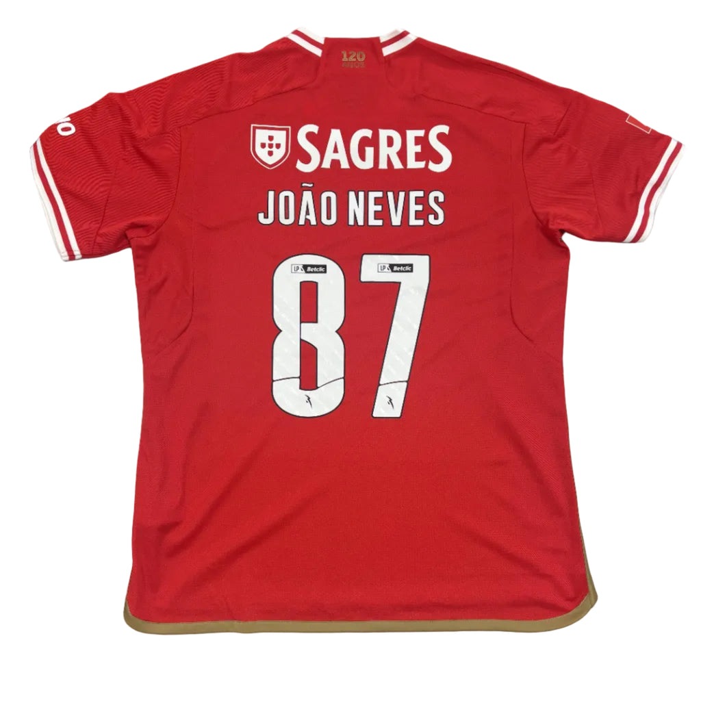 Red sports jersey with 'SAGRES' and 'JOÓ NEVES 87' printed on it, displayed on a round white surface.