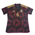 Black and red sports jersey with gold accents on a white surface, surrounded by packaging.